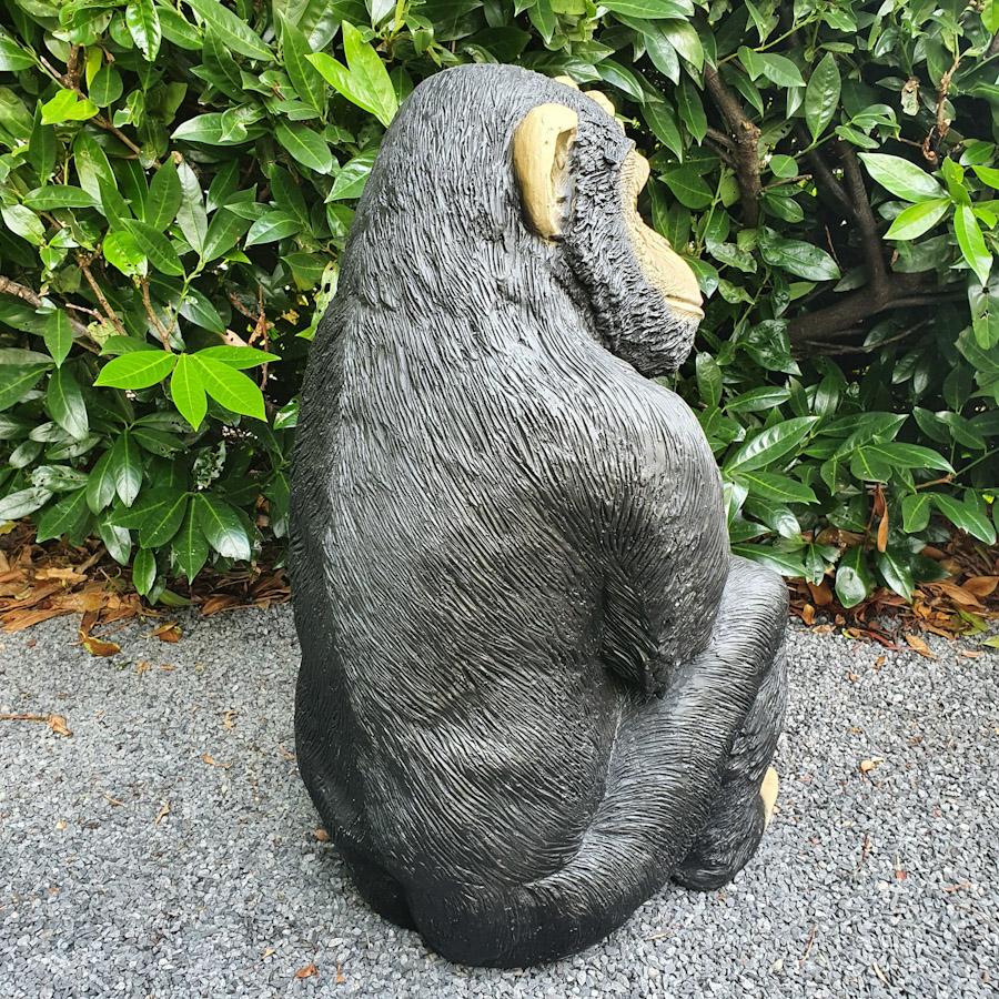Grosser Shimpanse kratzt sich am Kopf als Gartenfigur von hinten