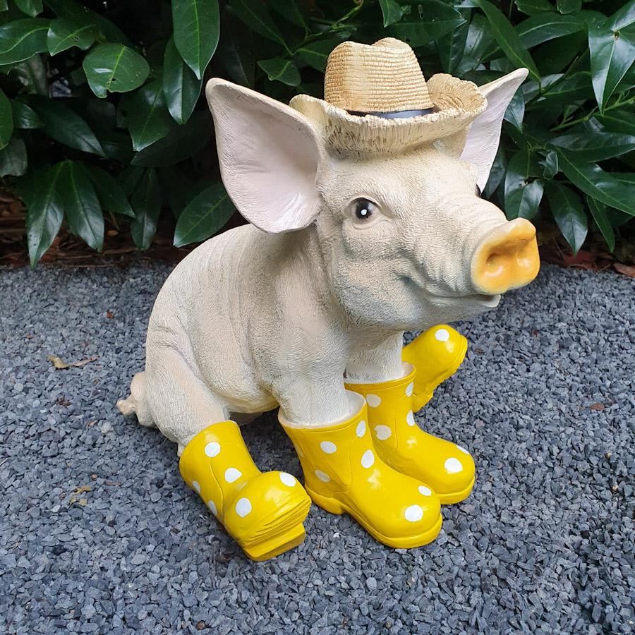 Sitzendes Schwein mit Hut und gelben Stiefeln als Gartenfigur
