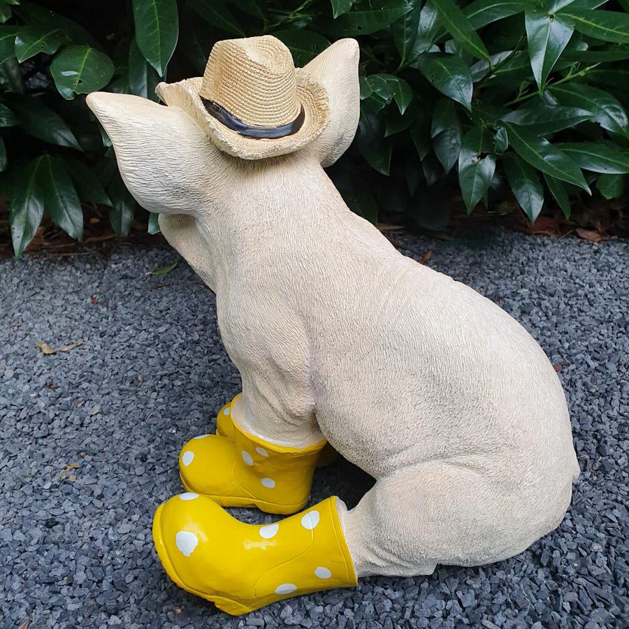 Sitzendes Schwein mit Hut und gelben Stiefeln als Gartenfigur von hinten