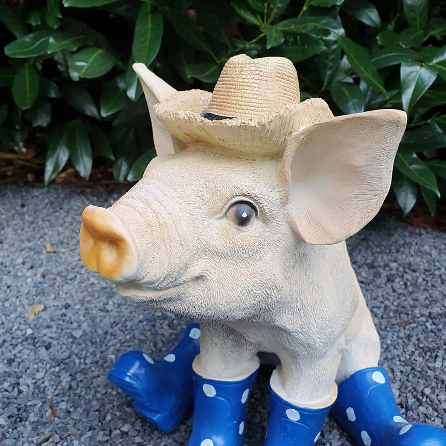Sitzendes Schwein mit Hut und blauen Stiefeln als Gartenfigur Nahaufnahme vom Kopf