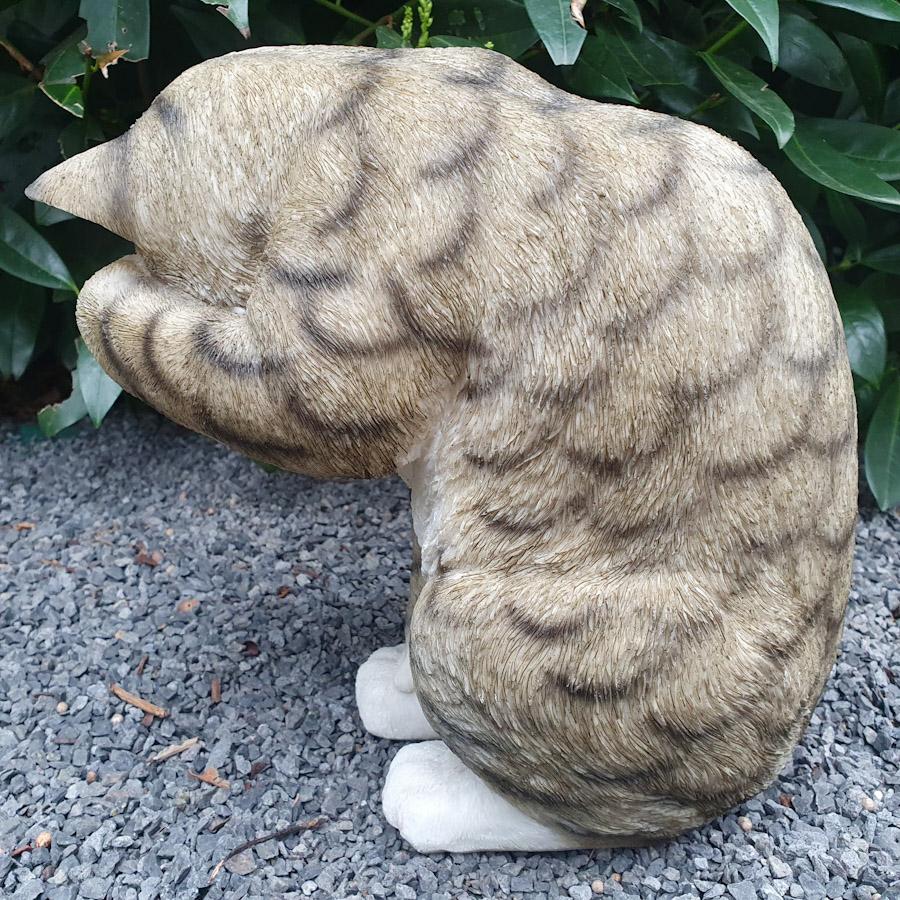 Sich putzende graue Katze als Gartenfigur von hinten
