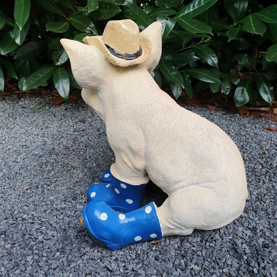 Sitzendes Schwein mit Hut und blauen Stiefeln als Gartenfigur von hinten