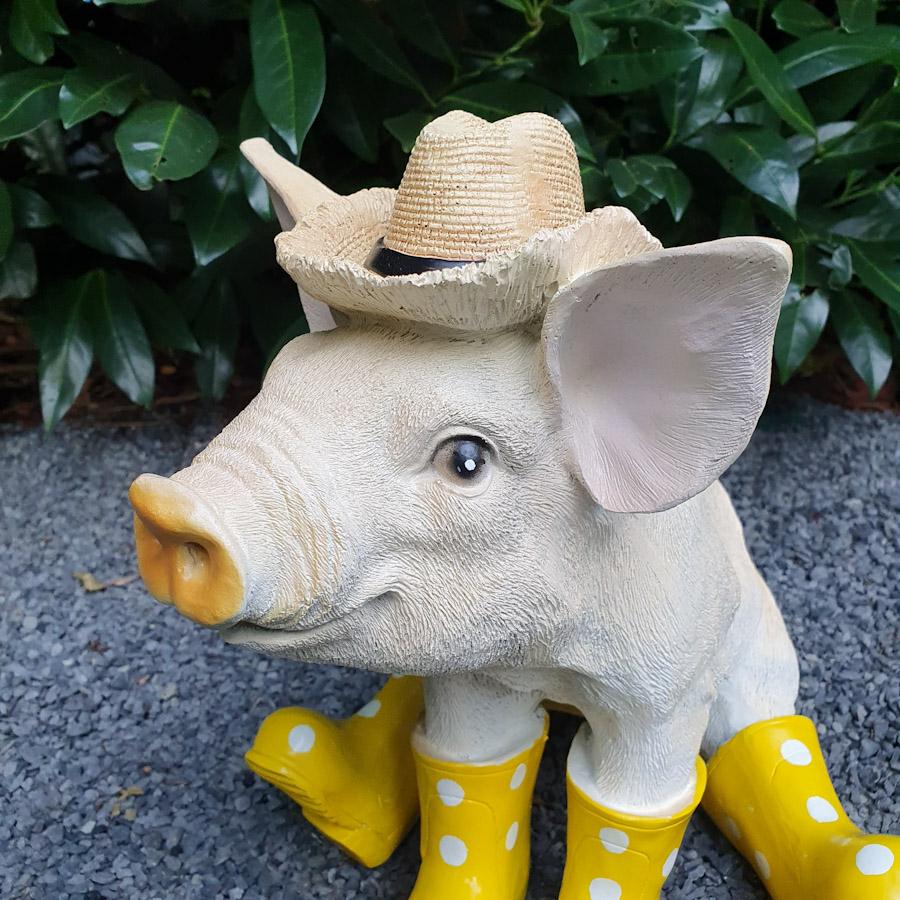 Sitzendes Schwein mit Hut und gelben Stiefeln als Gartenfigur Nahaufnahme vom Kopf