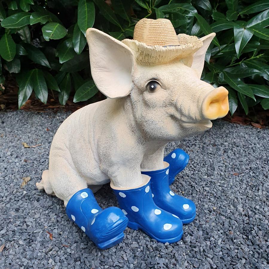 Sitzendes Schwein mit Hut und blauen Stiefeln als Gartenfigur