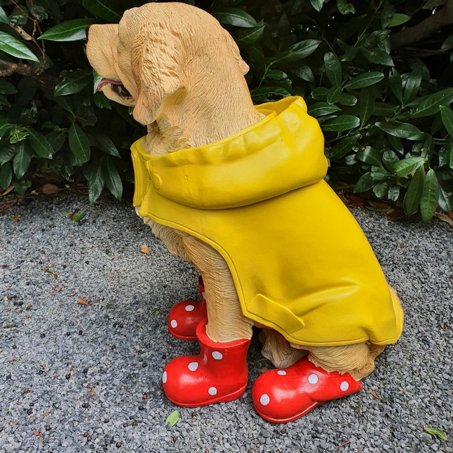Heller Labrador in Gelben Mantel und Roten Schuhen als Gartenfigur von hinten